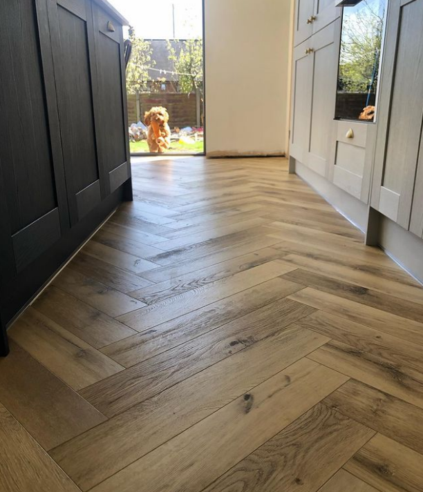 an image of herringbone laminate flooring in a kitchen, with a dog running into the room