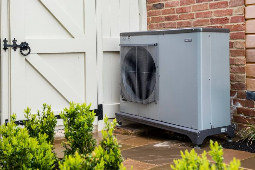grey air source heat pump next to white shed