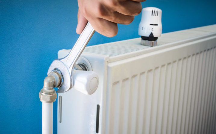 an image of a man using wrench to twist the radiator off the wall