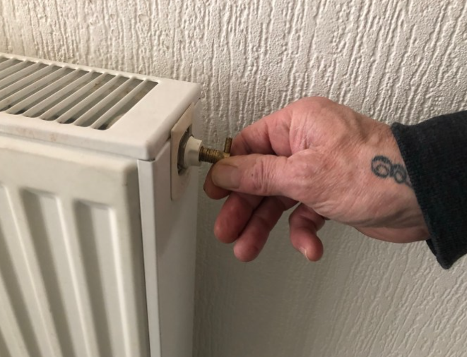 an image of a man twisting the bleed valve of the radiator
