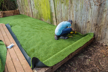 An image showing a man installing the artificial grass. He is cutting the edges against the garden fencing.