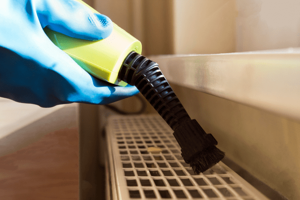 an image of a man using vacuum cleaner to clean behind radiator