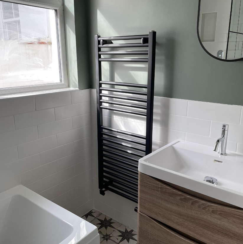 an image of a black ladder rail in a sage green coloured bathroom.