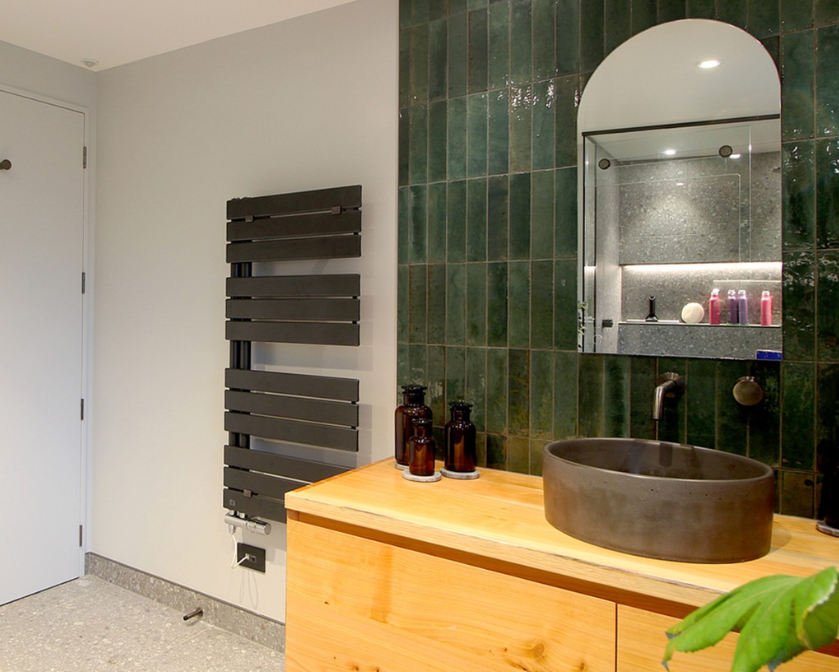 an image of a black modern towel rail in a bathroom. Sage green wall and black sink and mirror.